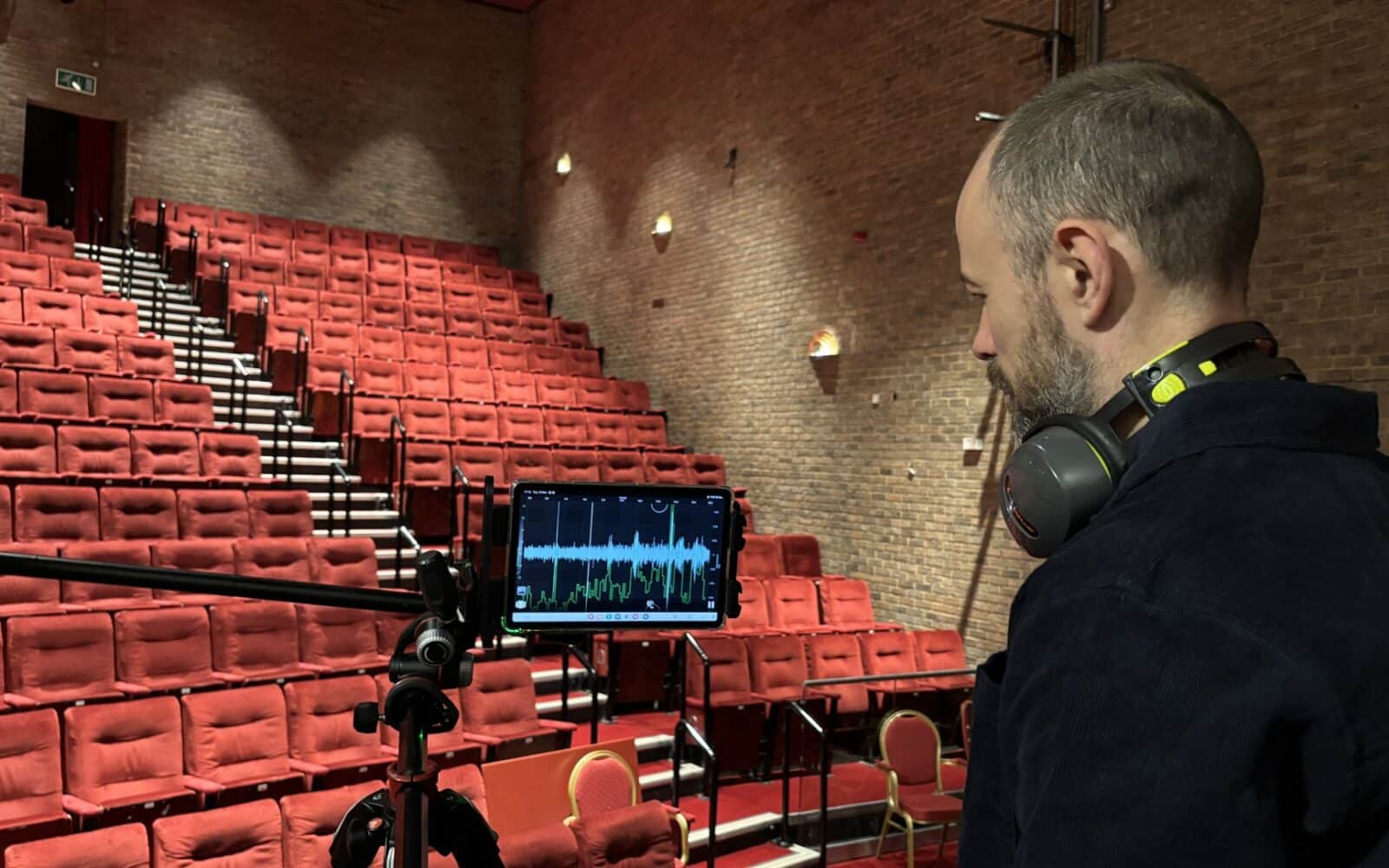 Sound engineer monitoring audio levels on tablet in Kenneth Moore Theatre auditorium during acoustics assessment.