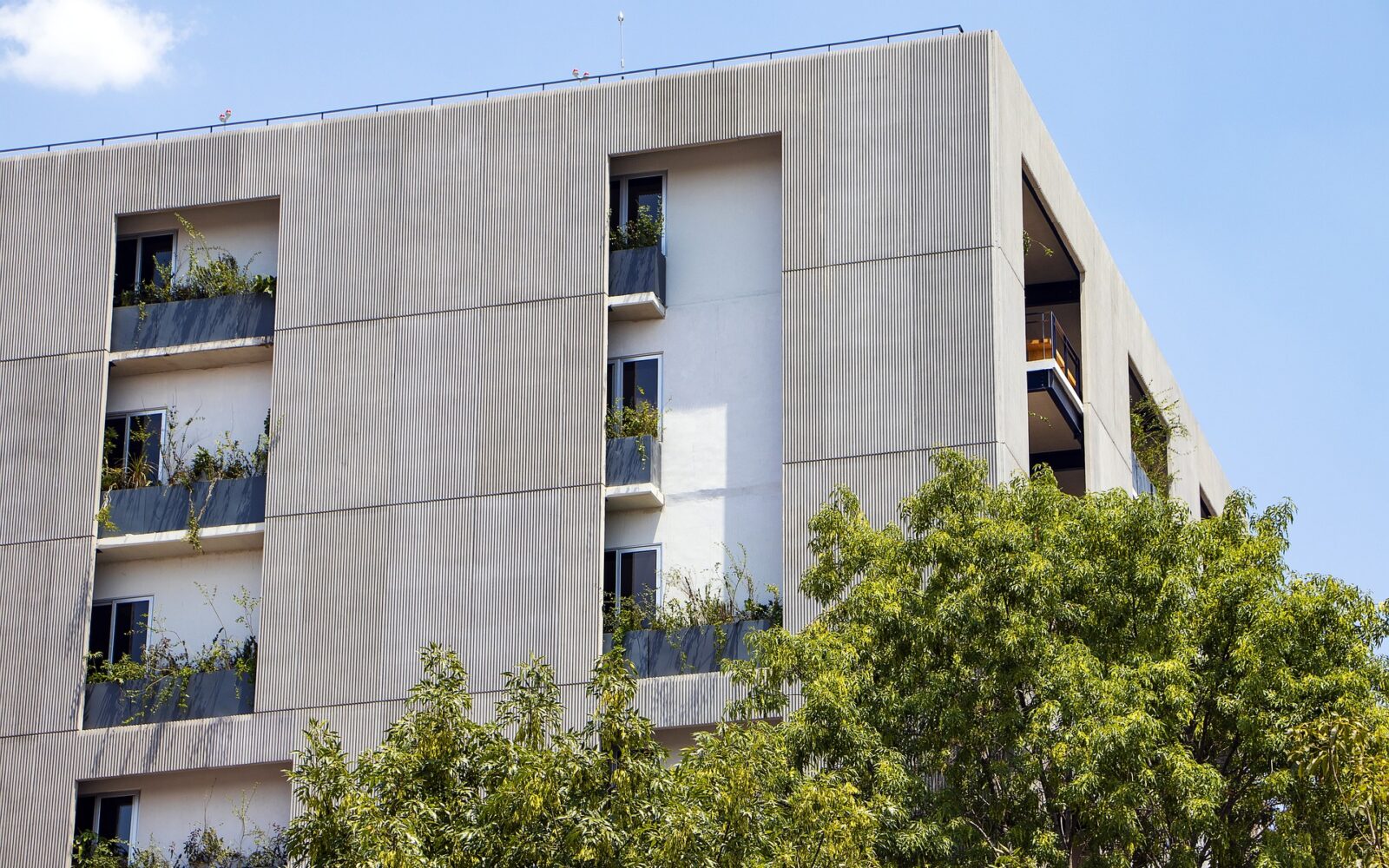 Modern apartment building with corrugated metal cladding, balconies, and integrated greenery demonstrating sustainable construction design principles.