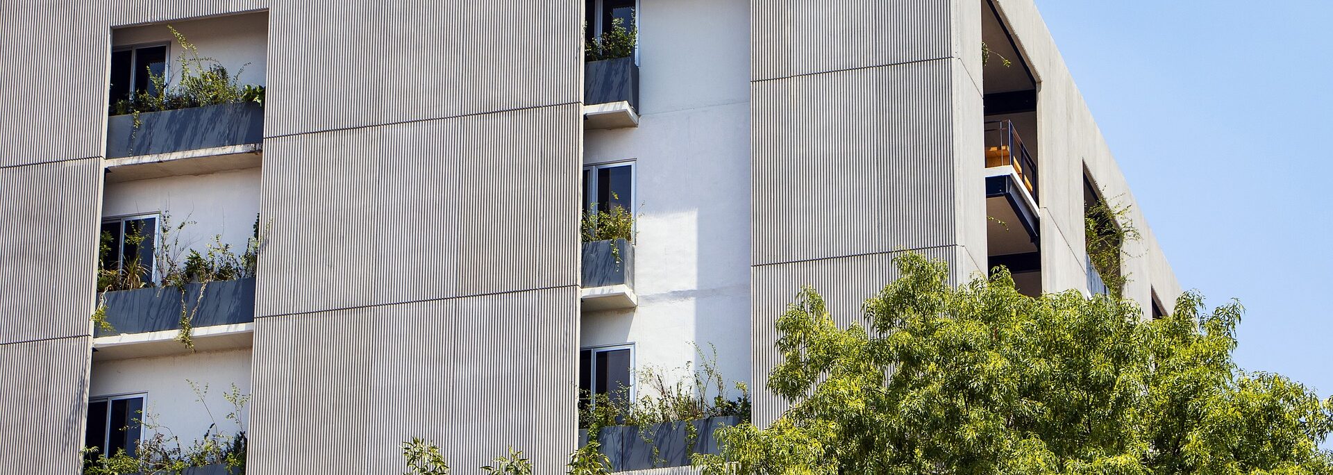 Modern apartment building with corrugated metal cladding, balconies, and integrated greenery demonstrating sustainable construction design principles.