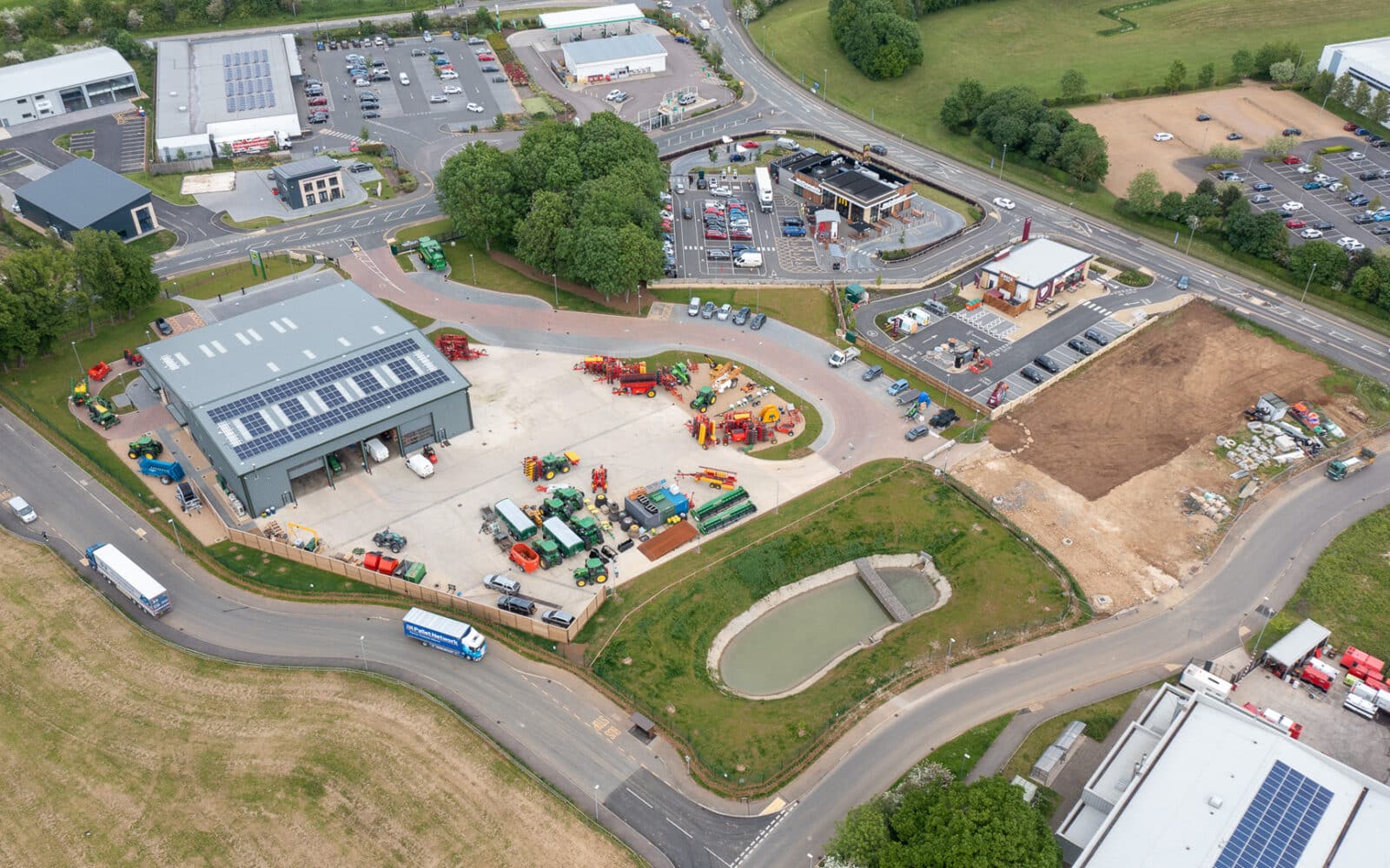 Aerial view of Oakham industrial site featuring agricultural equipment storage facility with solar panels, parking areas, and landscaped grounds.