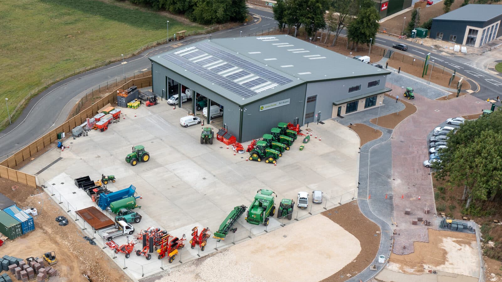 Agricultural equipment dealership facility in Oakham featuring green tractors, red machinery, and modern warehouse with solar panels.