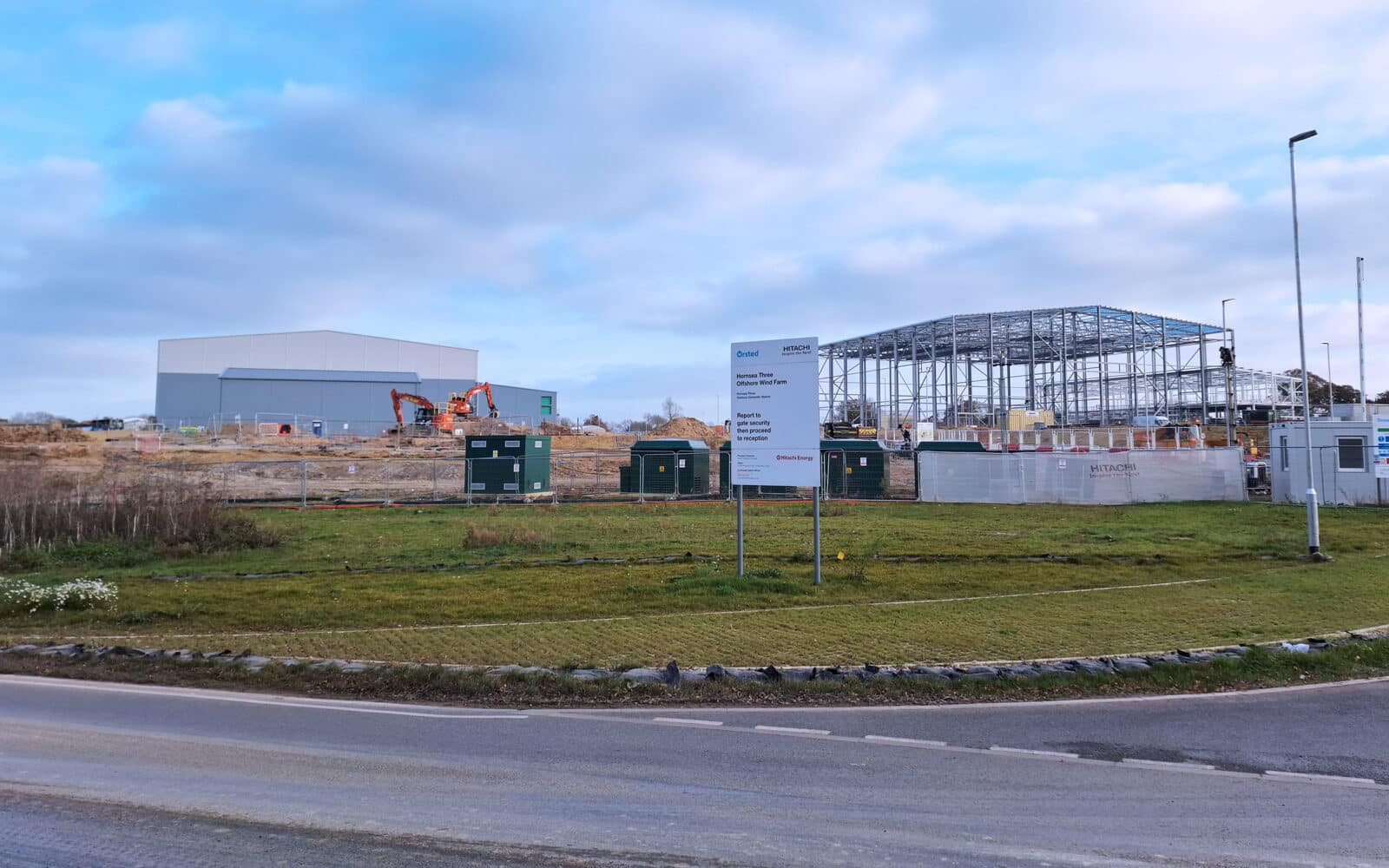 Construction site with steel-frame building under development, temporary facilities, and earthmoving equipment on green field.