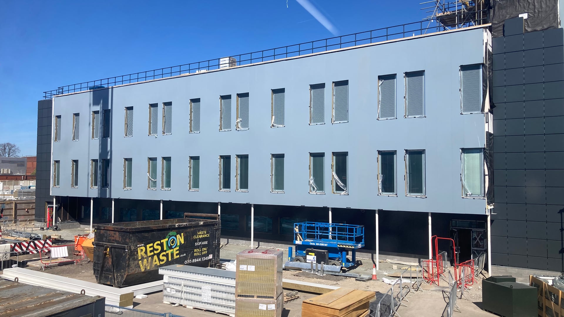 A three-story building under construction with covered windows, waste containers, and materials scattered in the foreground—monitored by an Associate of Noise Consultants to ensure compliance with sound regulations.