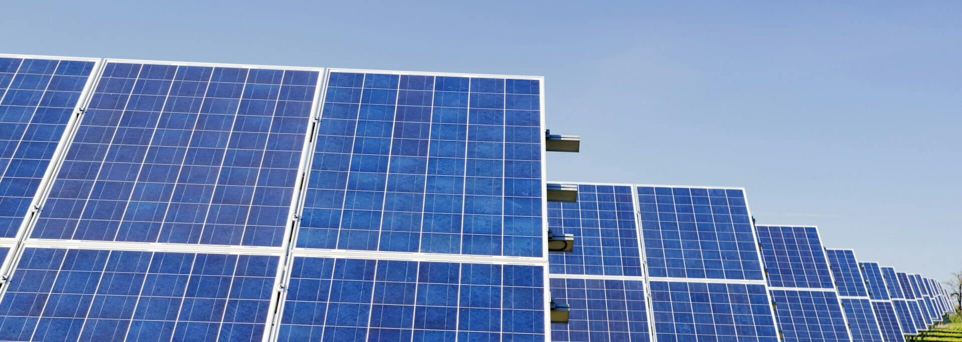 Solar panels mounted on metal frames in rows across a green field under clear sky